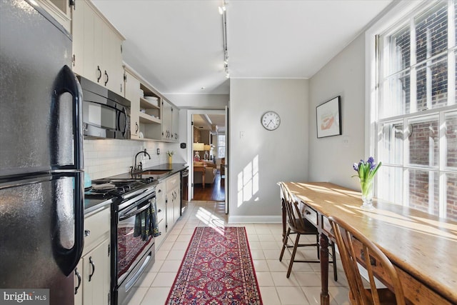 kitchen with tasteful backsplash, dark countertops, light tile patterned floors, black appliances, and a sink