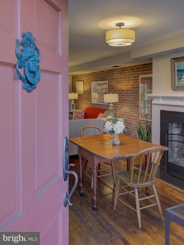 dining room featuring wood finished floors, a fireplace, brick wall, and ornamental molding