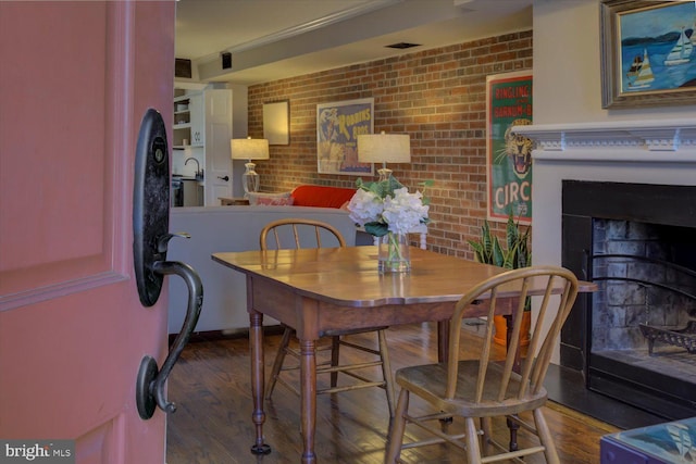 dining area featuring brick wall, wood finished floors, and a fireplace