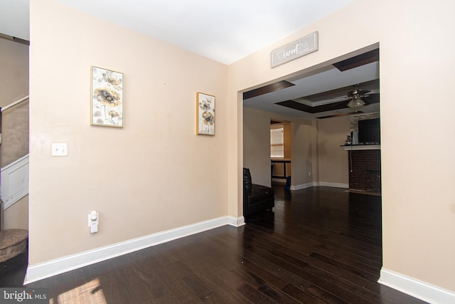 corridor featuring baseboards, a tray ceiling, and wood-type flooring