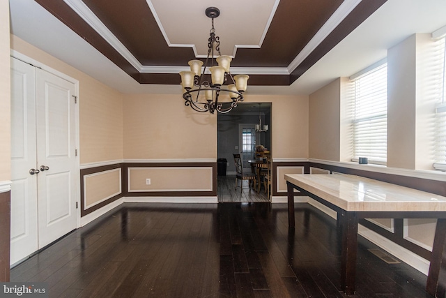 dining area with a raised ceiling, an inviting chandelier, wainscoting, and hardwood / wood-style flooring