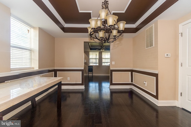 unfurnished dining area with visible vents, a notable chandelier, a tray ceiling, dark wood-style floors, and crown molding