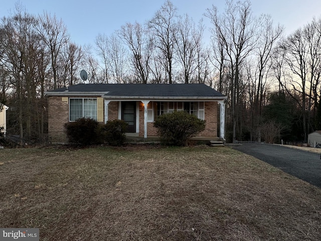 ranch-style home featuring brick siding, covered porch, and a front lawn