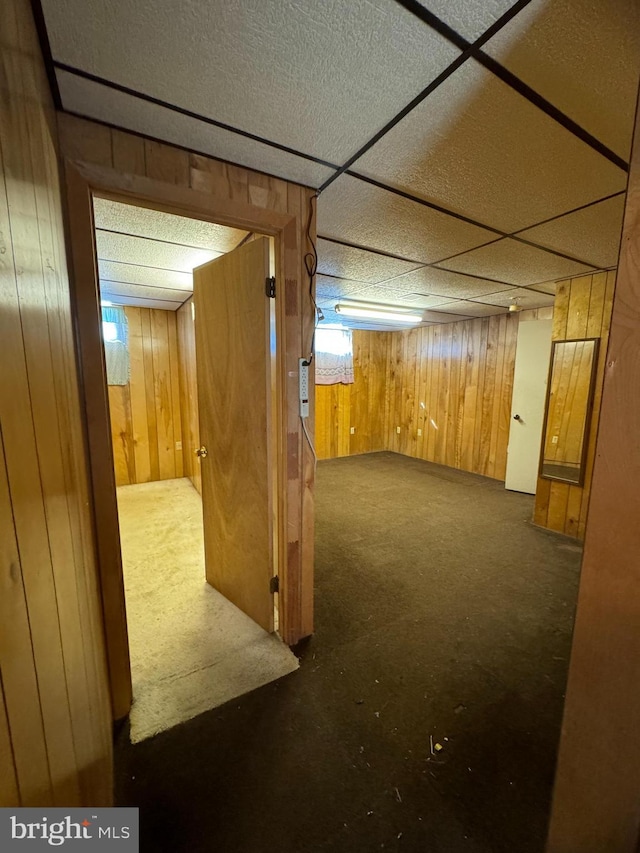 finished below grade area with a paneled ceiling, carpet, and wood walls