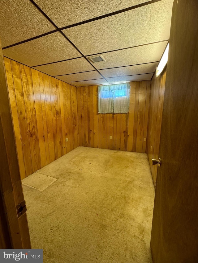 basement with wooden walls, carpet flooring, a paneled ceiling, and visible vents