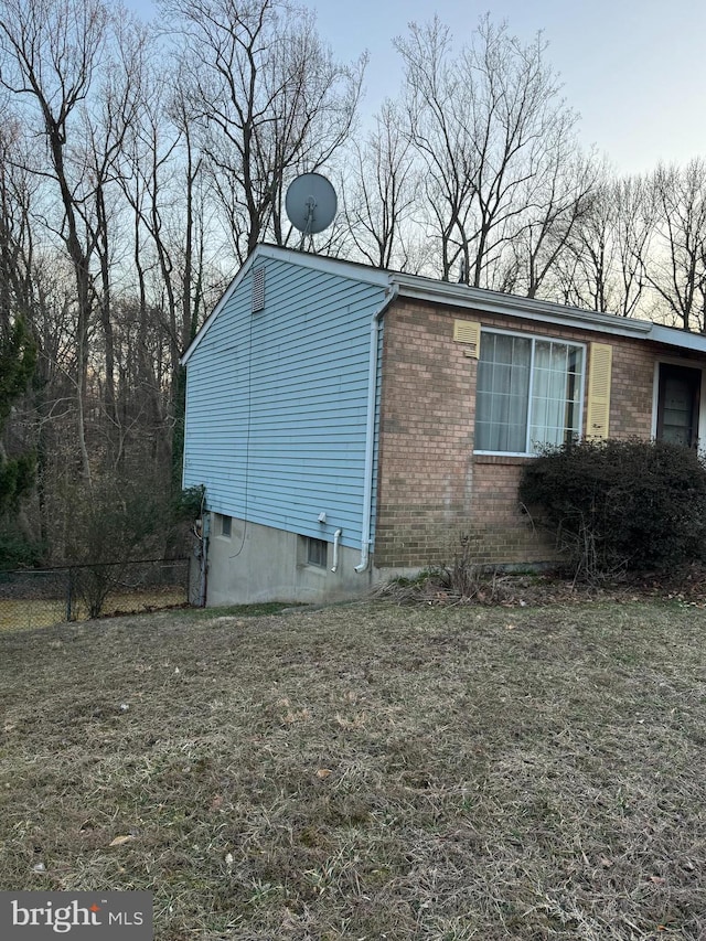 view of side of home featuring a yard, fence, and brick siding