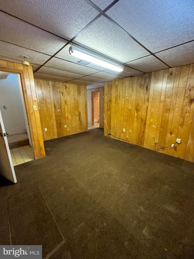 finished below grade area with carpet flooring, a paneled ceiling, and wooden walls