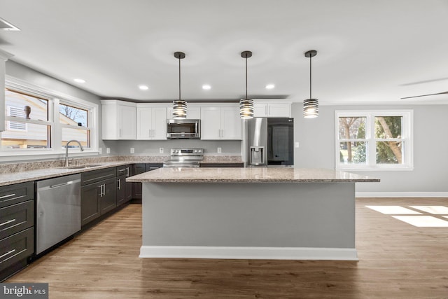 kitchen with a kitchen island, light wood-style flooring, a sink, white cabinets, and appliances with stainless steel finishes