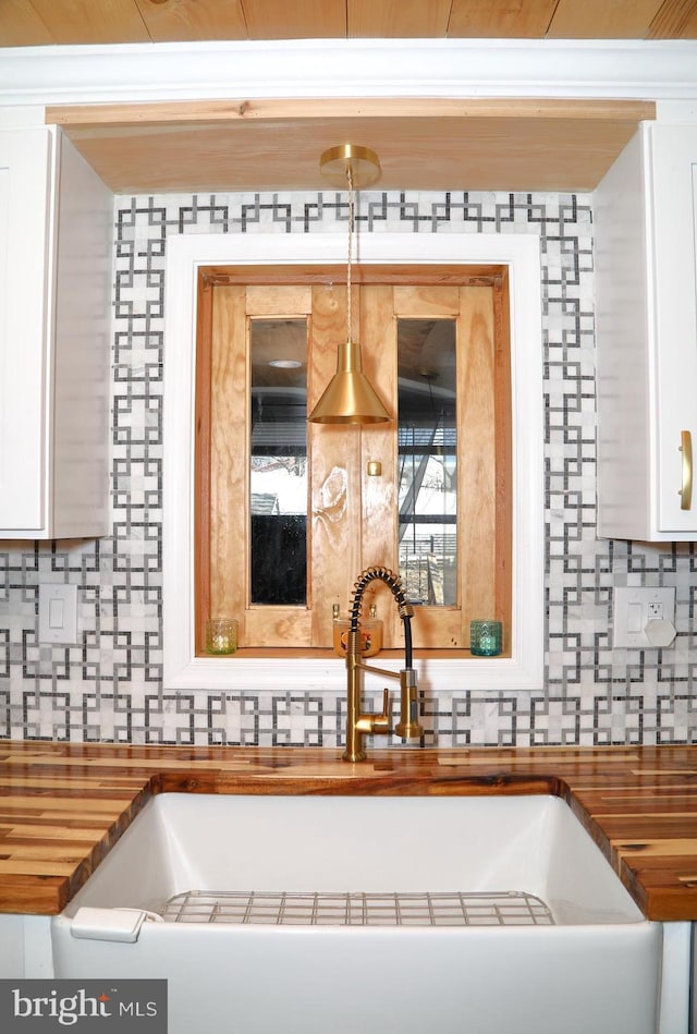 kitchen featuring a sink, wood counters, decorative backsplash, and white cabinetry