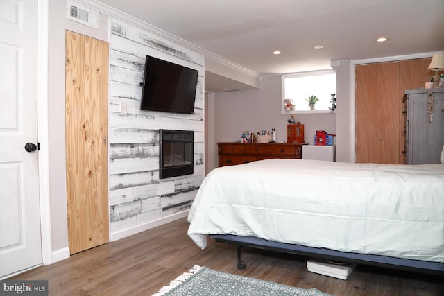 bedroom featuring visible vents, ornamental molding, wood finished floors, a large fireplace, and baseboards