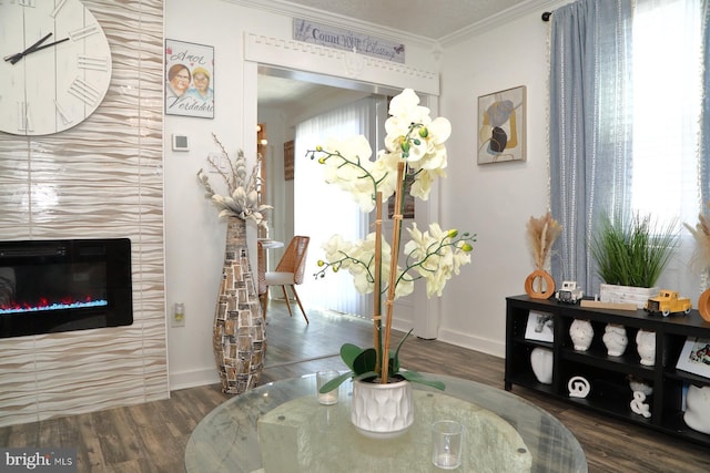 interior space with a glass covered fireplace, crown molding, baseboards, and wood finished floors