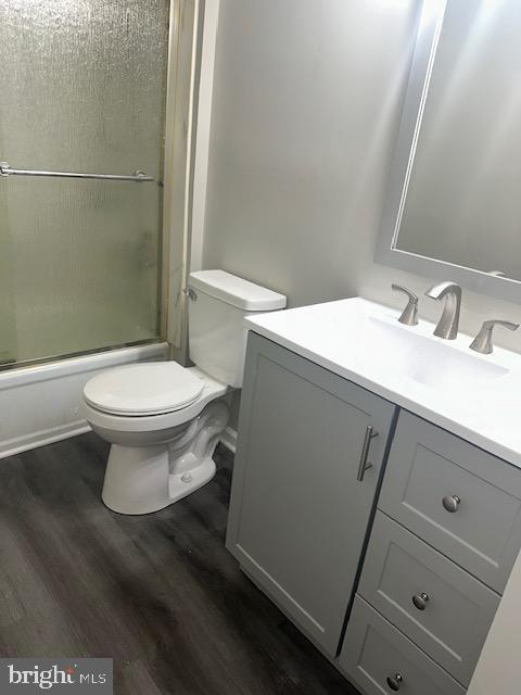 full bathroom featuring bath / shower combo with glass door, toilet, wood finished floors, and vanity