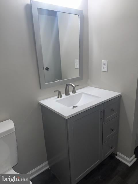 half bath with toilet, vanity, baseboards, and wood finished floors