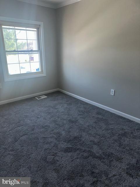 unfurnished room with dark colored carpet, visible vents, baseboards, and crown molding