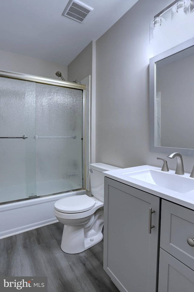 full bath with visible vents, toilet, wood finished floors, combined bath / shower with glass door, and vanity