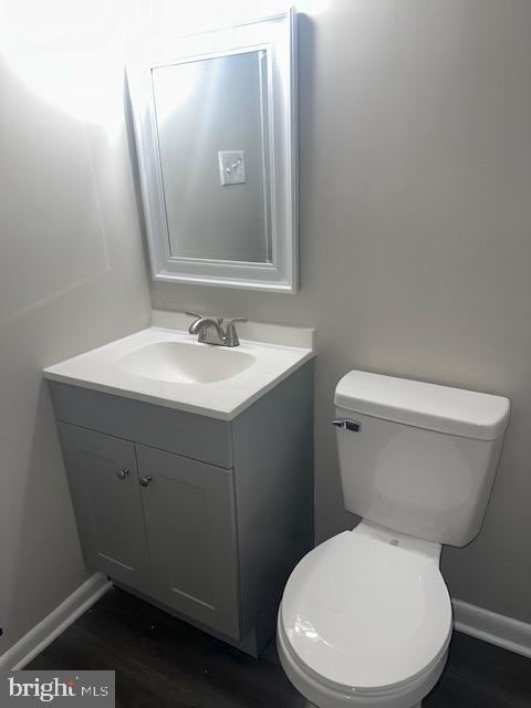 half bathroom featuring toilet, vanity, baseboards, and wood finished floors