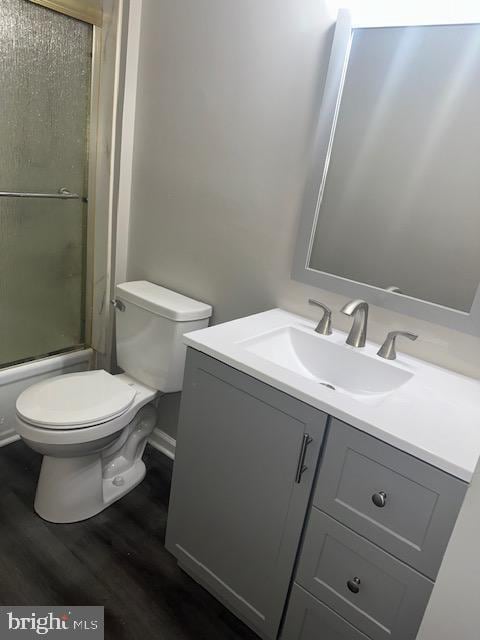 bathroom with bath / shower combo with glass door, toilet, wood finished floors, and vanity