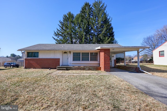 ranch-style home featuring brick siding, a front lawn, fence, a carport, and driveway