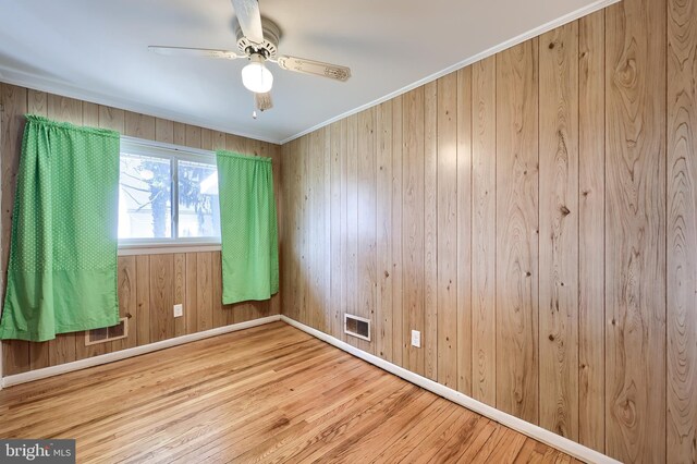 unfurnished room with wood finished floors, baseboards, visible vents, ceiling fan, and ornamental molding