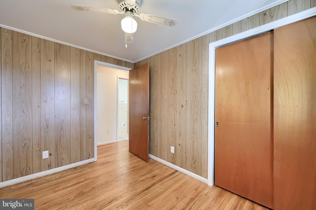 unfurnished bedroom with wooden walls, baseboards, ornamental molding, wood finished floors, and a closet