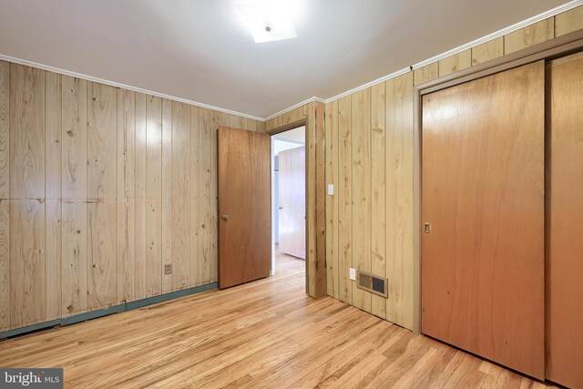 unfurnished bedroom with wood finished floors, visible vents, a closet, wood walls, and crown molding