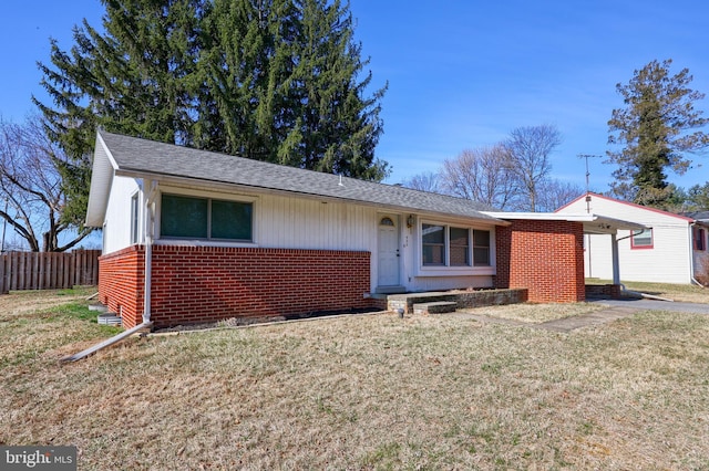 ranch-style home with a front yard, fence, brick siding, and roof with shingles