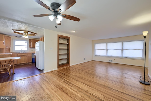 unfurnished living room with visible vents, baseboards, built in features, hardwood / wood-style flooring, and a sink