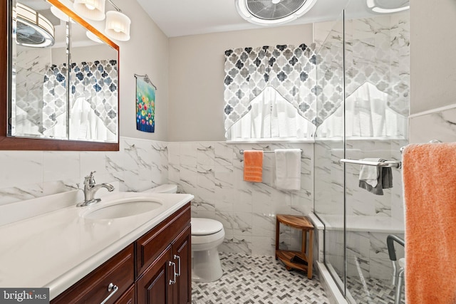 full bath with toilet, a marble finish shower, tile walls, wainscoting, and vanity