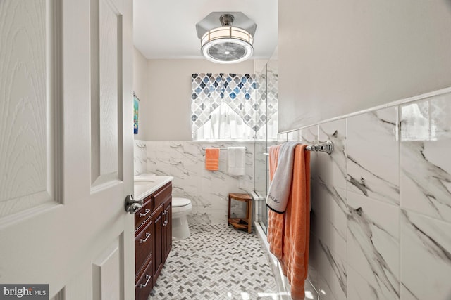 full bath featuring vanity, a wainscoted wall, a marble finish shower, tile walls, and toilet