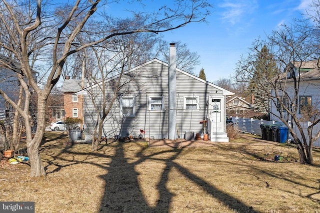 back of house featuring a lawn, a chimney, and fence