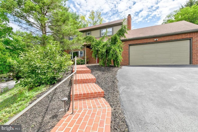 view of front of house featuring a chimney, brick siding, an attached garage, and driveway