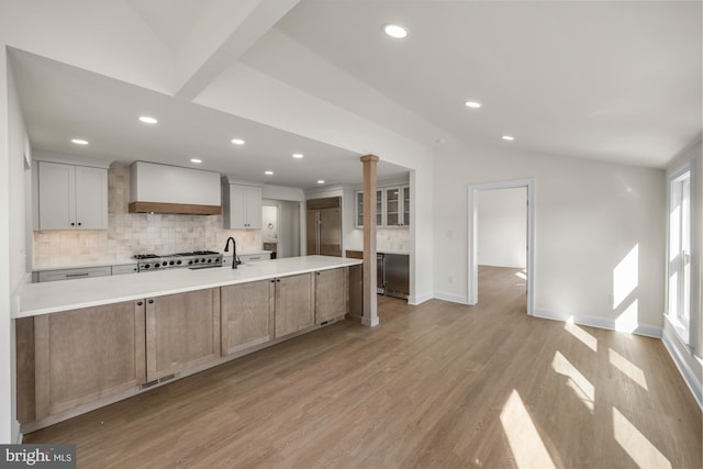 kitchen with custom range hood, backsplash, appliances with stainless steel finishes, light wood finished floors, and lofted ceiling