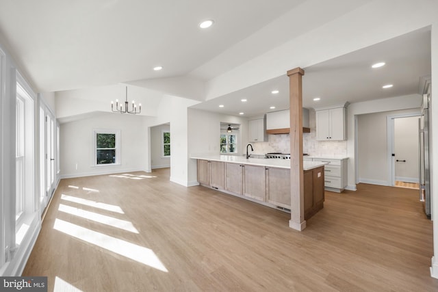 kitchen featuring light wood finished floors, open floor plan, light countertops, lofted ceiling, and a sink