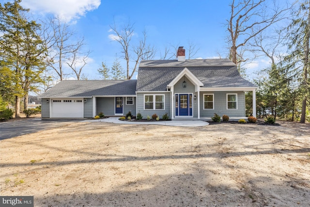 dutch colonial featuring a chimney, a garage, driveway, and roof with shingles