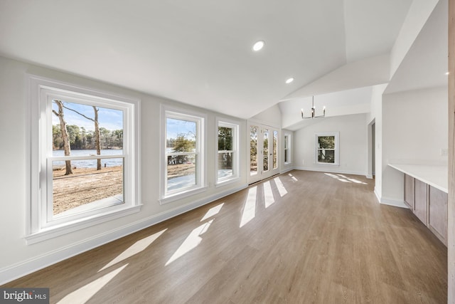 unfurnished living room with vaulted ceiling, a notable chandelier, light wood-style floors, and baseboards