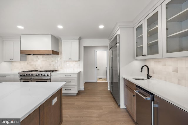 kitchen featuring premium range hood, light wood-style floors, white cabinetry, high end appliances, and a sink