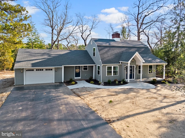 colonial inspired home with a gambrel roof, driveway, roof with shingles, an attached garage, and a chimney