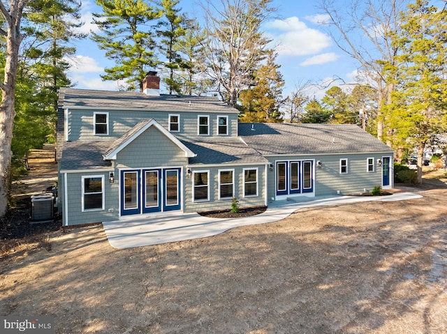 rear view of house with cooling unit, a shingled roof, a chimney, and a patio area