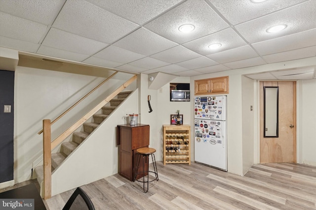 bar featuring stairway, light wood-style flooring, a paneled ceiling, and freestanding refrigerator