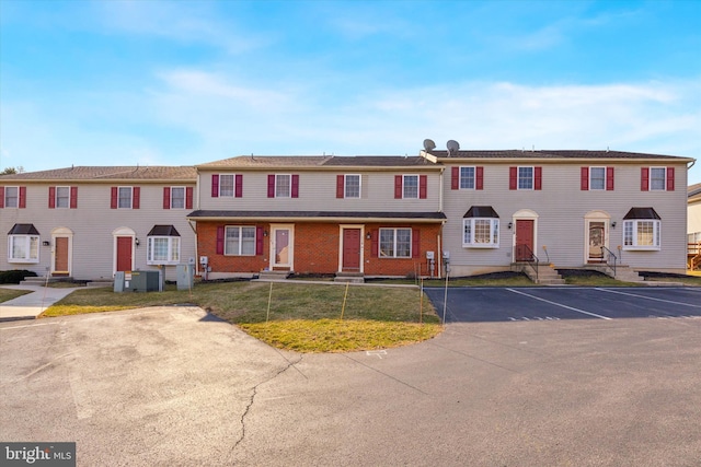 view of property featuring central AC unit, uncovered parking, a front lawn, and entry steps