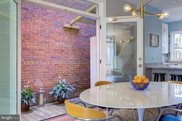 dining space featuring wood finished floors, brick wall, and a chandelier