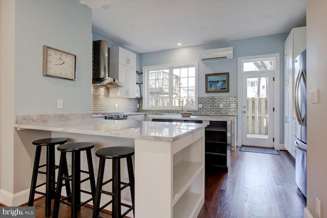 kitchen featuring a wall mounted air conditioner, wall chimney range hood, open shelves, and a peninsula