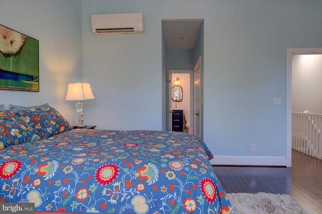 bedroom featuring wood-type flooring, ensuite bath, an AC wall unit, and baseboards