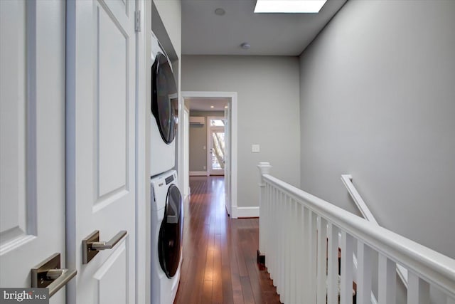 washroom featuring stacked washer and clothes dryer, baseboards, laundry area, and dark wood finished floors