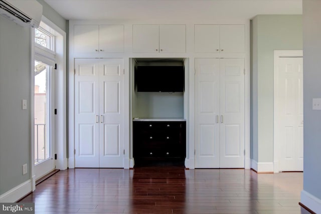unfurnished bedroom with baseboards, multiple closets, a wall mounted AC, and wood finished floors
