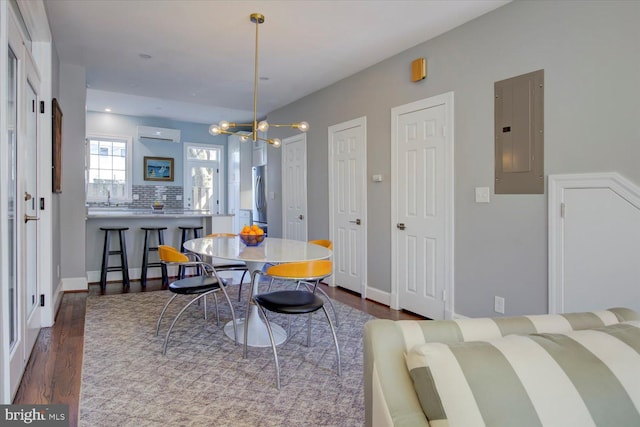 dining area featuring a wall unit AC, dark wood-style flooring, baseboards, a chandelier, and electric panel