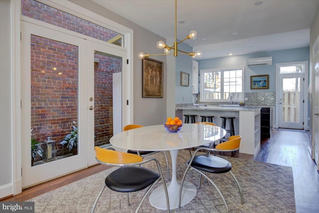 dining room featuring a wall mounted AC, a notable chandelier, brick wall, and wood finished floors