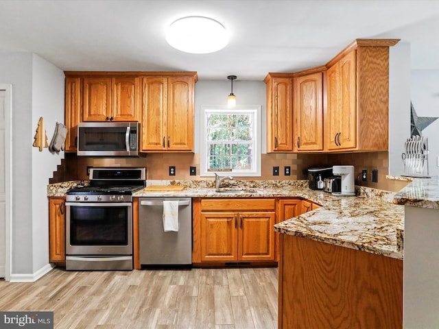 kitchen featuring light stone counters, light wood-style flooring, stainless steel appliances, and brown cabinets