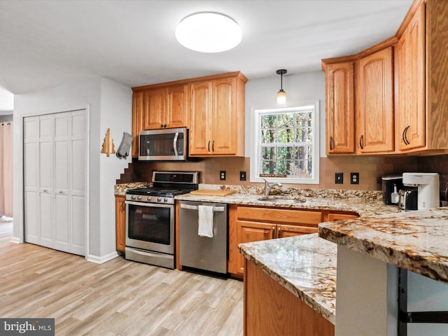 kitchen featuring light wood-style flooring, a sink, light stone counters, backsplash, and appliances with stainless steel finishes