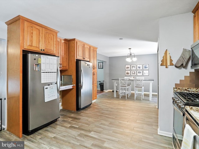 kitchen with pendant lighting, stainless steel appliances, light wood finished floors, baseboards, and a chandelier